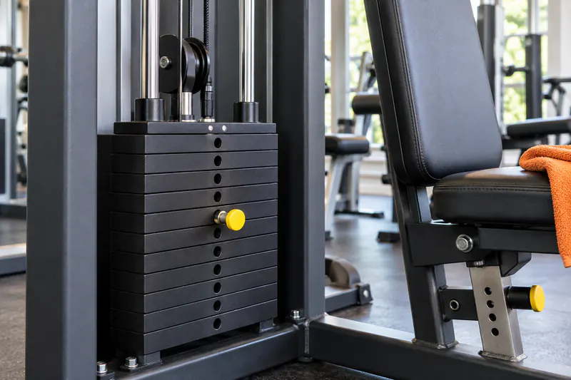 Een gewichtstapel met insteekpen naast de verstelbare zitting van een fitnessapparaat